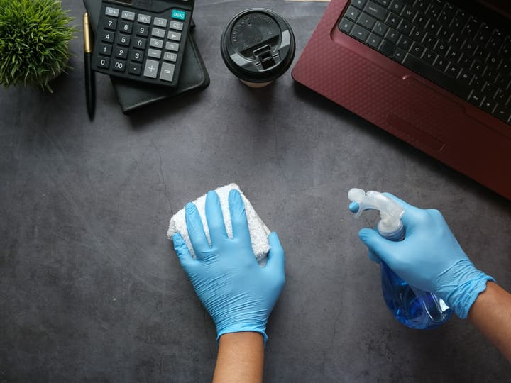 Igienizzazione di una scrivania in un ufficio a Trento con guanti e detergente